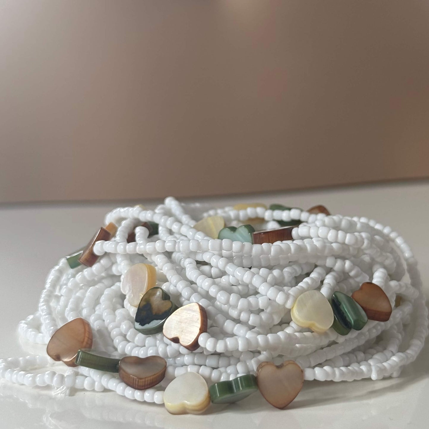waist beads with white beads and heart-shaped multicoloured stones on a light background