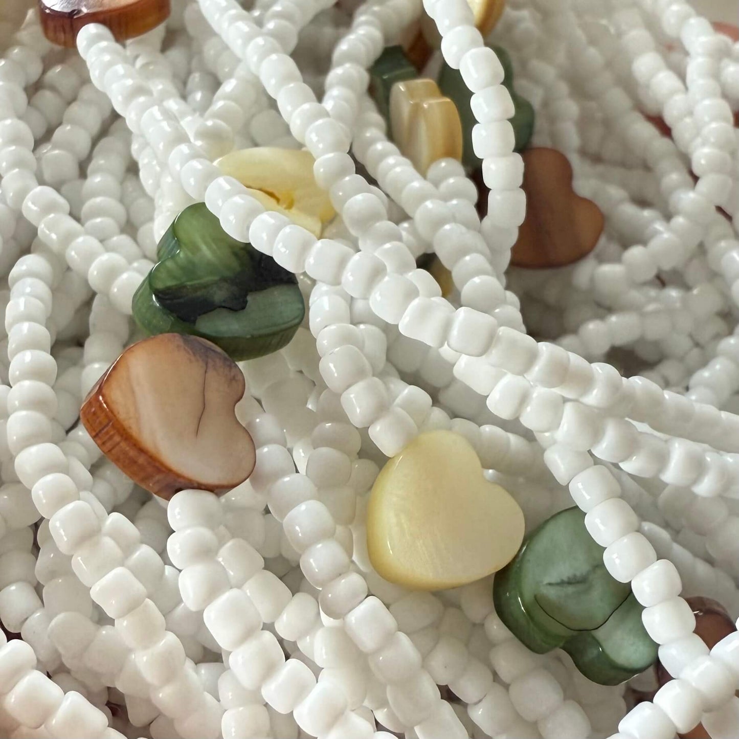 waist beads with white beads and heart-shaped multicolored stones on a light background